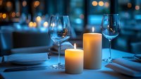 Romantic restaurant table setting with glowing candles and wine glasses against blurred blue bokeh background creates intimate dining atmosphere.