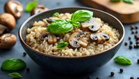 Creamy mushroom risotto garnished with fresh basil leaves in dark ceramic bowl, served with sliced champignon mushrooms on rustic blue background.