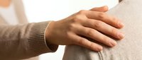 Caring hand gently placed on someone's shoulder, expressing empathy, support, and comfort in a warm, neutral-toned setting.