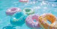 Colorful frosted donuts with sprinkles floating in bright blue swimming pool water on sunny summer day, creating playful and refreshing food photography composition.