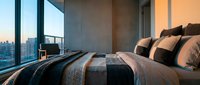 Luxury bedroom with striped bedding and decorative pillows overlooking urban skyline through floor-to-ceiling windows, suitable for hospitality and interior design projects.
