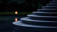 Minimalist curved stone steps in twilight with soft orange sun reflection on dark water surface creating moody atmospheric scene.