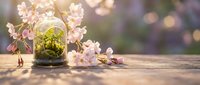 Spring cherry blossom branches with moss in glass jar on wooden table with warm bokeh lights creating cozy seasonal home decor atmosphere.