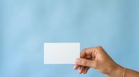 Hand holding blank white business card against soft blue background, suitable for branding, corporate identity, and marketing presentations.