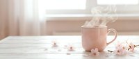 Steaming pink ceramic mug on white wooden table with delicate cherry blossom flowers in soft morning light, cozy spring atmosphere.
