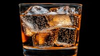 Cold refreshing carbonated drink with ice cubes in glass against dark background, bubbles rising through amber liquid creating dynamic texture and sparkle.