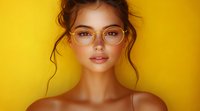 Young Asian woman wearing stylish transparent glasses against vibrant yellow background, natural makeup and messy updo hairstyle for beauty and fashion concepts.