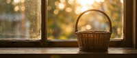 Empty wicker basket on wooden windowsill with warm golden sunlight streaming through glass panes creating cozy autumn atmosphere for home decor and seasonal displays.