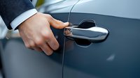 Male hand in business suit opening modern car door handle against dark blue vehicle exterior. Luxury automotive detail for dealership and sales concepts.