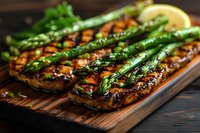 Grilled salmon fillets topped with fresh asparagus spears and lemon on wooden cutting board, glazed with honey-soy marinade, close up view of gourmet dinner.