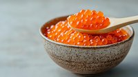 Fresh red caviar in ceramic bowl with wooden spoon, bright orange salmon roe against blurred background. Luxury seafood delicacy for gourmet cuisine.