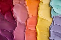 Colorful smeared cosmetic texture in rainbow gradient from burgundy to pastel purple, creamy makeup swatches showing smooth consistency and rich pigmentation.