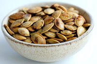 Roasted pumpkin seeds in a ceramic bowl on white background, ready for snacking, cooking, or nutritional content use.