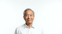 Senior Asian man with gray hair wearing light blue button-up shirt, smiling warmly at camera against white background for corporate portraits and professional headshots.