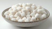 White sugar cubes piled in rustic ceramic bowl against neutral background, minimalist food styling for culinary and lifestyle content.