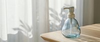Glass pump bottle with clear liquid on wooden surface in bright natural light with soft shadows from window curtains for skincare and wellness products.