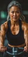 Confident mature Asian woman with silver hair in black sportswear exercising at gym. Strong athletic female doing strength training workout showing muscular arms and determination.