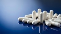 White pharmaceutical capsules scattered on reflective blue surface for medical healthcare and medication concepts.