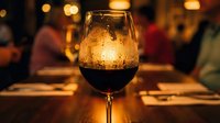 Red wine glass with condensation droplets on warm restaurant table with golden bokeh lights creating cozy dining atmosphere for romantic evening celebration.