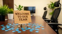 Wooden welcome sign on office desk with blue confetti for new employee onboarding and team integration in modern workplace environment.