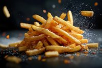 Crispy golden french fries sprinkled with salt particles in dynamic motion against dark background. Close-up shot with selective focus captures seasoning moment.