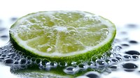 Fresh lime slice with water drops on dark surface, macro photography showing citrus texture and juicy pulp detail in bright natural lighting.