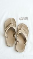 Pair of beige canvas flip-flop sandals with frayed edges on white background with slow life text for lifestyle and wellness concepts.