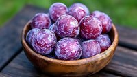 Fresh ripe purple plums covered with natural bloom in rustic wooden bowl on dark wooden table, selective focus, macro food photography.