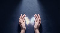 Hands gently cupping glowing white butterfly symbolizing transformation, hope, freedom and spiritual growth on dark textured background for wellness concepts.