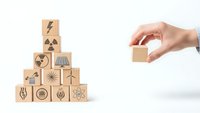 Hand placing wooden cube with energy icons in pyramid formation representing renewable power sources and sustainable technology solutions.