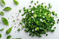 Fresh chopped green onions scattered on white background with basil leaves and black pepper, overhead view. Perfect for cooking, food blogs and culinary projects.