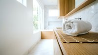 Rolled white towel on wooden shelf in modern bathroom with marble backsplash and natural light from window, suitable for spa and hospitality design projects.