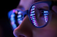 Close-up view of eyeglasses reflecting digital screen with programming code, capturing modern technology lifestyle in purple and blue neon lighting.