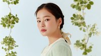 Young Asian woman with natural makeup and hair ribbon against light background with green botanical elements, suitable for beauty and fashion campaigns.