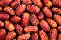 Fresh red dates background with natural wrinkled texture and glossy surface, close up view of dried sweet fruits arranged in rows showing organic pattern.
