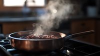Sizzling meat in copper pan on gas stove with rising steam and smoke, dramatic lighting in dark rustic kitchen setting creates appetizing cooking atmosphere.