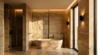 Modern luxury bathroom interior with marble walls, freestanding bathtub, warm lighting and natural stone textures creating spa-like atmosphere for home design.