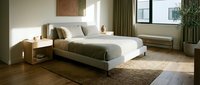 Modern bedroom with neutral tones features a platform bed with olive green bedding, wooden nightstands, and natural light from large windows. Interior design.