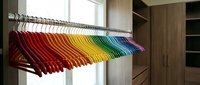 Colorful rainbow hangers arranged in gradient order on closet rod in modern walk-in wardrobe with wooden shelving and natural light from window.