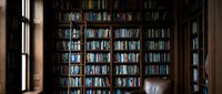 Cozy home library with floor-to-ceiling bookshelves filled with books, leather armchair and natural window light creating warm reading atmosphere.