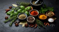 Fresh herbs and colorful spices arranged on dark slate surface with mortar and pestle for culinary cooking and seasoning food preparation.