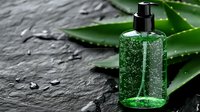 Green transparent gel bottle with pump dispenser on dark stone surface with fresh aloe vera leaves and water drops, natural skincare concept.