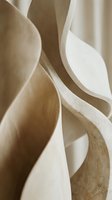 Abstract wooden sculpture with flowing organic curves and natural grain patterns creating artistic shadows and depth in warm neutral tones.