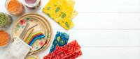 Colorful craft supplies and decorative materials arranged on white wooden surface, including beads, fabrics, and embellishments for DIY projects and creative hobbies.