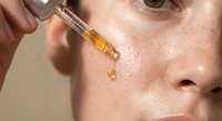 Young woman applying golden facial serum with dropper for skincare routine. Natural beauty treatment with oil essence for hydration and anti-aging care.