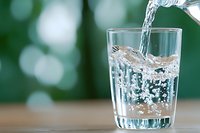 Fresh clean water pouring into transparent glass with dynamic splash and bubbles against blurred green bokeh background, refreshing drink concept.