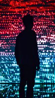 Silhouette of person against glowing red and blue digital background with bokeh light effects, creating dramatic contrast between dark figure and luminous display.