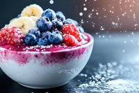 Vibrant smoothie bowl topped with fresh blueberries, raspberries, banana slices and powdered sugar in white ceramic bowl against dark background, healthy breakfast.