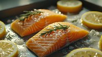 Fresh raw salmon fillets with rosemary sprigs and lemon slices on crushed ice, ready for cooking. Close up view shows rich orange color and marbled texture.