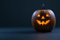 Glowing carved pumpkin with classic jack o'lantern face illuminated from within on dark background, creating spooky Halloween atmosphere.